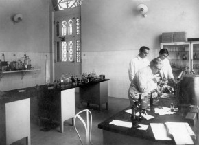 Oswaldo Cruz observa um microscópio ao lado de seu filho Bento e de Burle de Figueiredo, no interior de um dos laboratórios do Castelo de Manguinhos, 1910. Fonte: Acervo da Casa de Oswaldo Cruz.