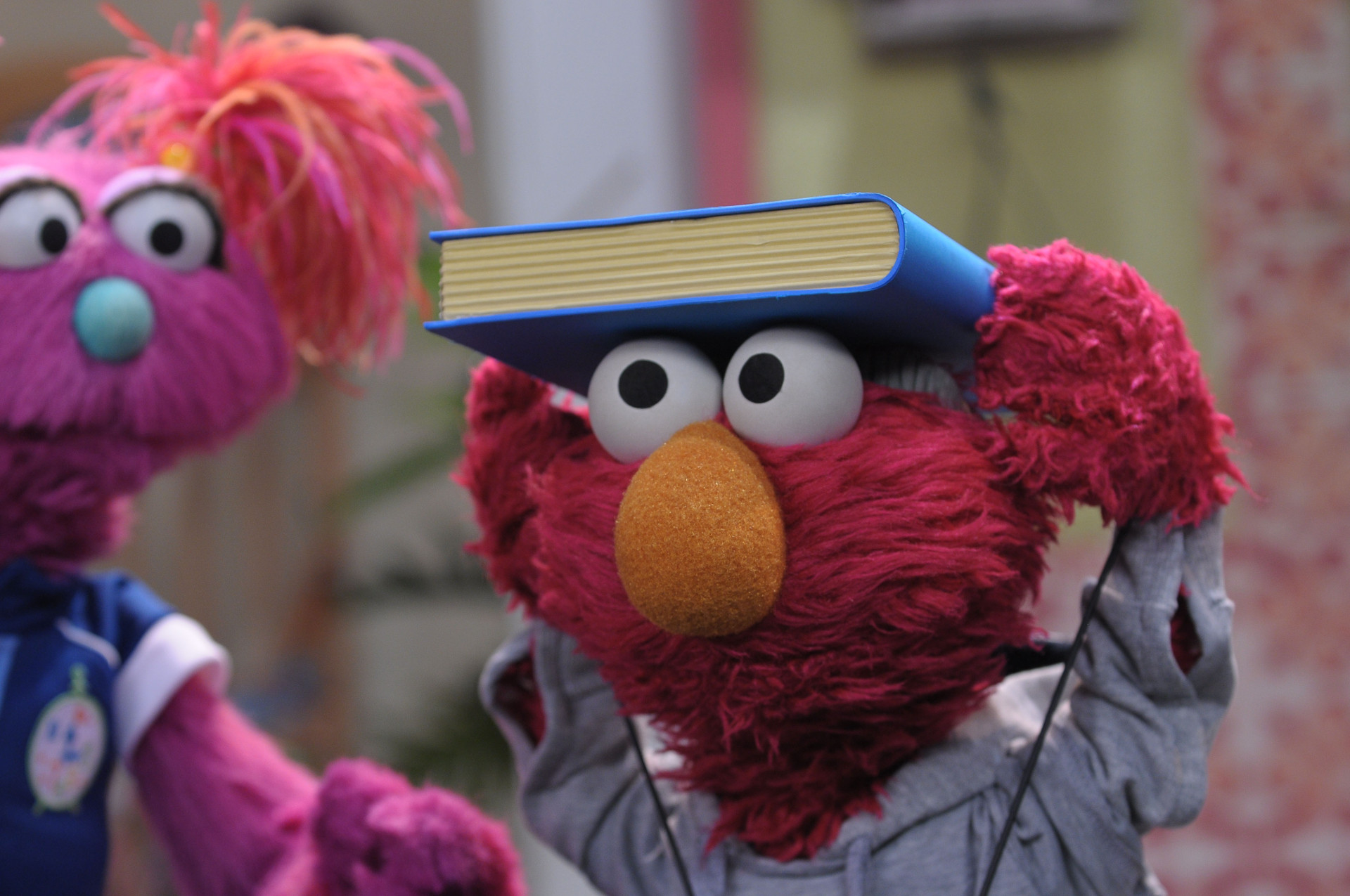 Elmo treina andar com um livro apoiado na cabeça