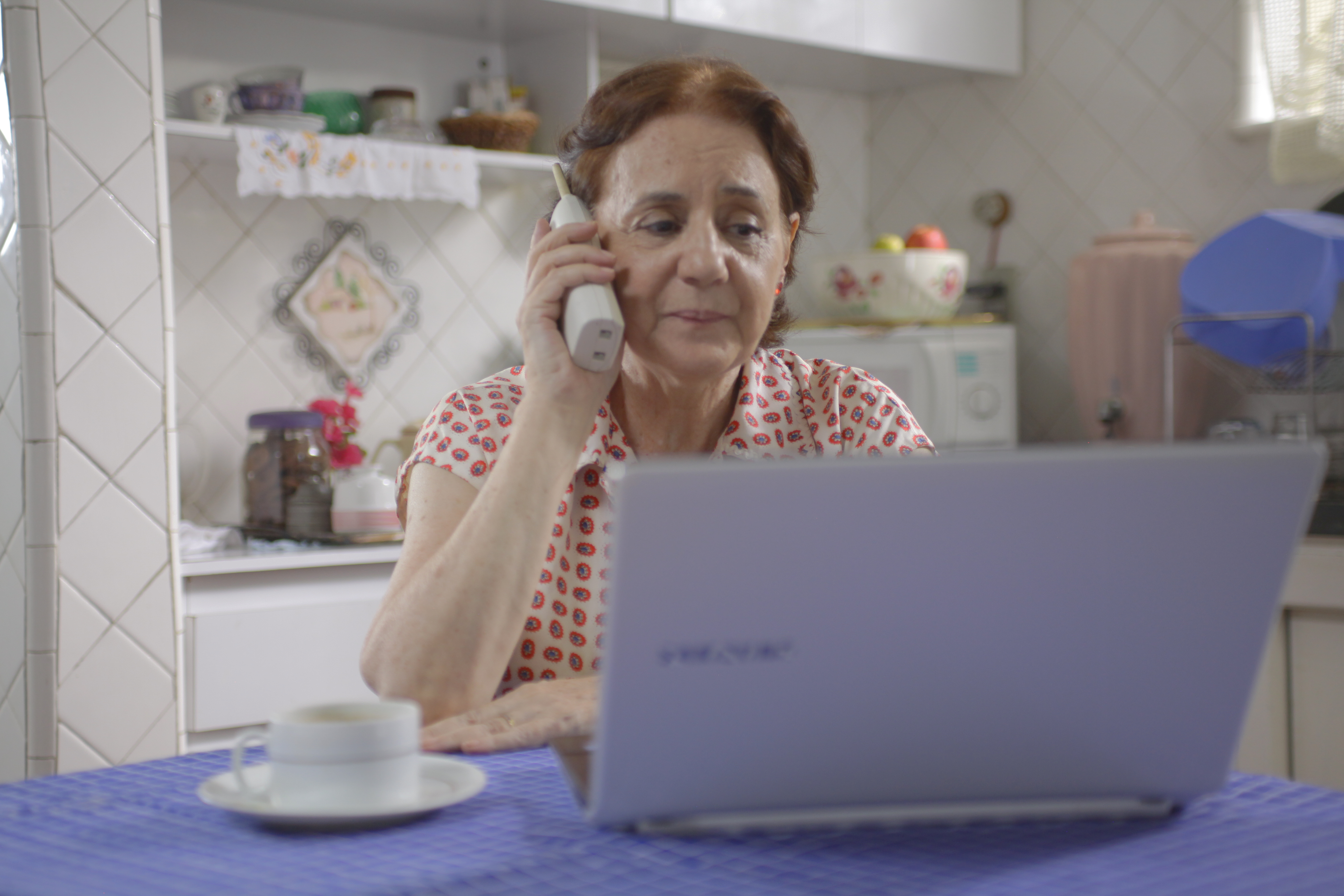 Mulher fala ao telefone e olha o computador