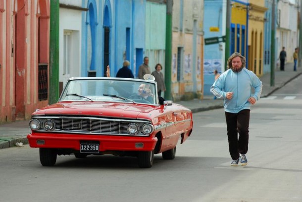 O empresário trapaceiro Orsini (no carro) e o ex-campeão Jacob Van Oppel (correndo) percorrem povoados do Uruguai em busca de combates clandestinos